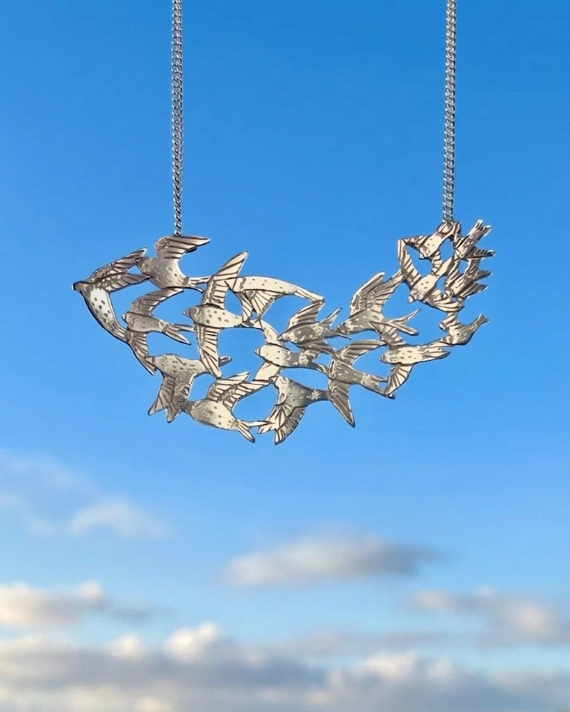 Handmade sterling silver statement pendant featuring a murmuration flock of seventeen hand-engraved birds in flight against a blue sky background