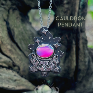 Oxidised sterling silver Cauldron Pendant with pink Aurora Opal and triple moon, hanging on its chain in woodland