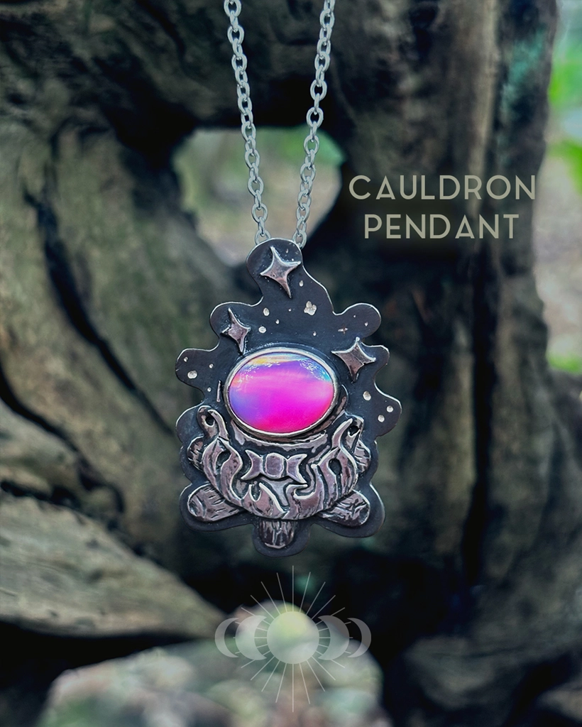 Oxidised sterling silver Cauldron Pendant with pink Aurora Opal and triple moon, hanging on its chain in woodland