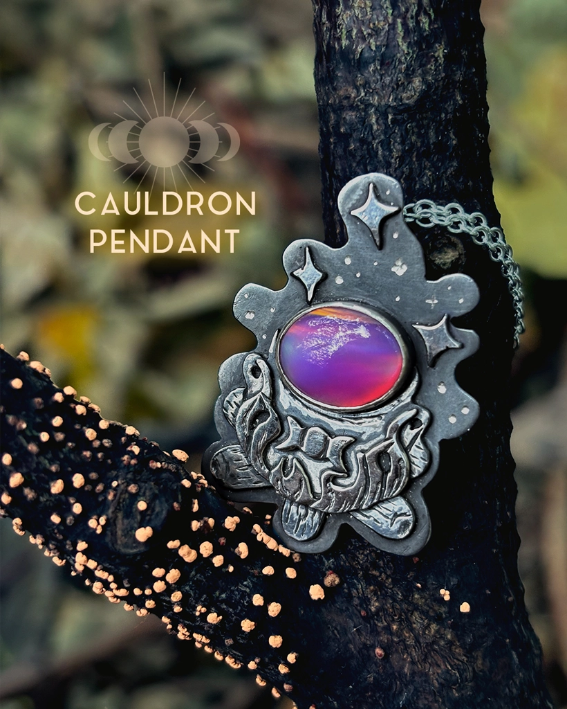 Oxidised sterling silver Cauldron Pendant with a purple Aurora Opal and engraved stars, styled against dark branches