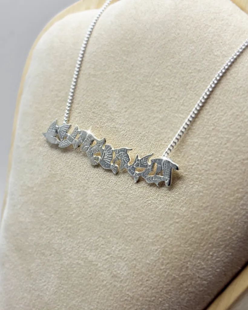 Front view of a handmade sterling silver bar necklace depicting a textured flock of flying birds, designed by Stacy Bias Jewellery on a cream display stand.