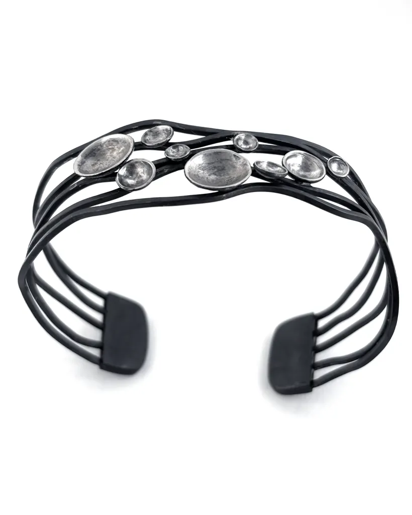 Open oxidised sterling silver cuff bracelet at an angle, wavy dark bands and flat terminals with a cluster of domes