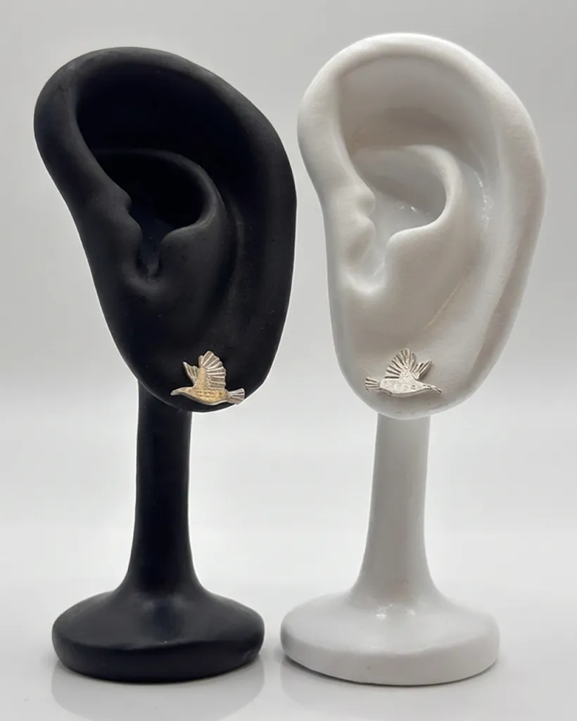 Sterling Silver Starling Stud Earring, Single Bird Stud A single sterling silver starling stud earring, an engraved bird in flight, shown on black and white display ears