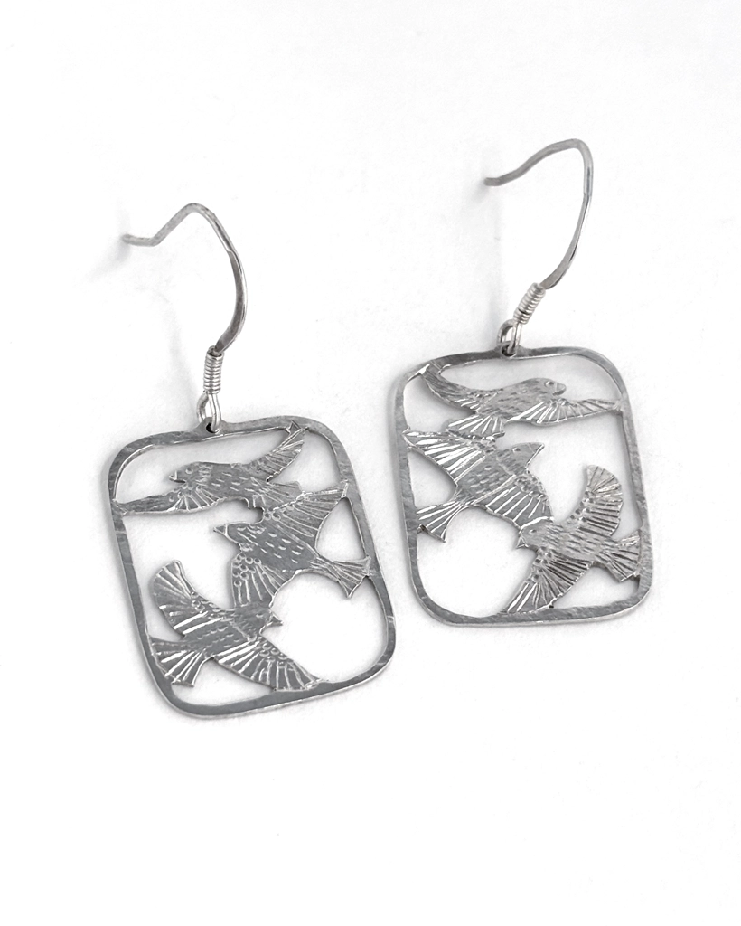 Pair of sterling silver three bird drop earrings laid flat, saw-pierced starlings in flight and hammered hooks