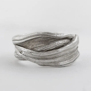 Side view of a chunky sterling silver wave ring, folded layered ridges running across a wide band, on white