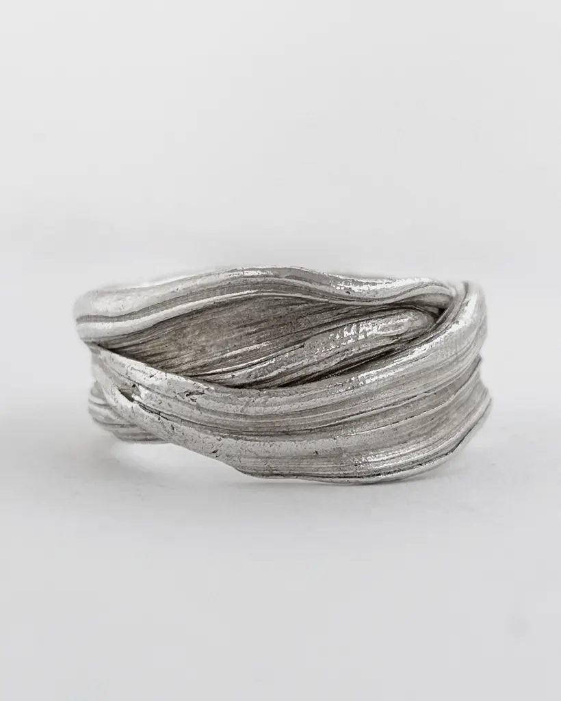 Side view of a chunky sterling silver wave ring, folded layered ridges running across a wide band, on white