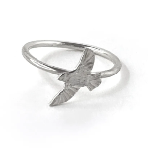 Single sterling silver bird ring on a slim band, an engraved bird in flight with downswept wings, on white