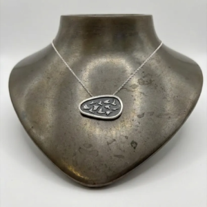 Artisan handmade sterling silver asymmetrical necklace with a flock of silver birds on an oxidized shield background, displayed on a dark metallic neck bust.