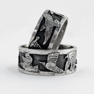 Two wide oxidised sterling silver starling band rings on white, bright raised birds in flight against a dark ground
