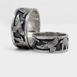 Two wide sterling silver bird rings with starlings in flight raised bright against an oxidised blackened band