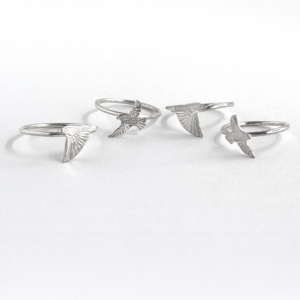 Four sterling silver starling rings laid out together, each an engraved starling in a different flying pose, on white