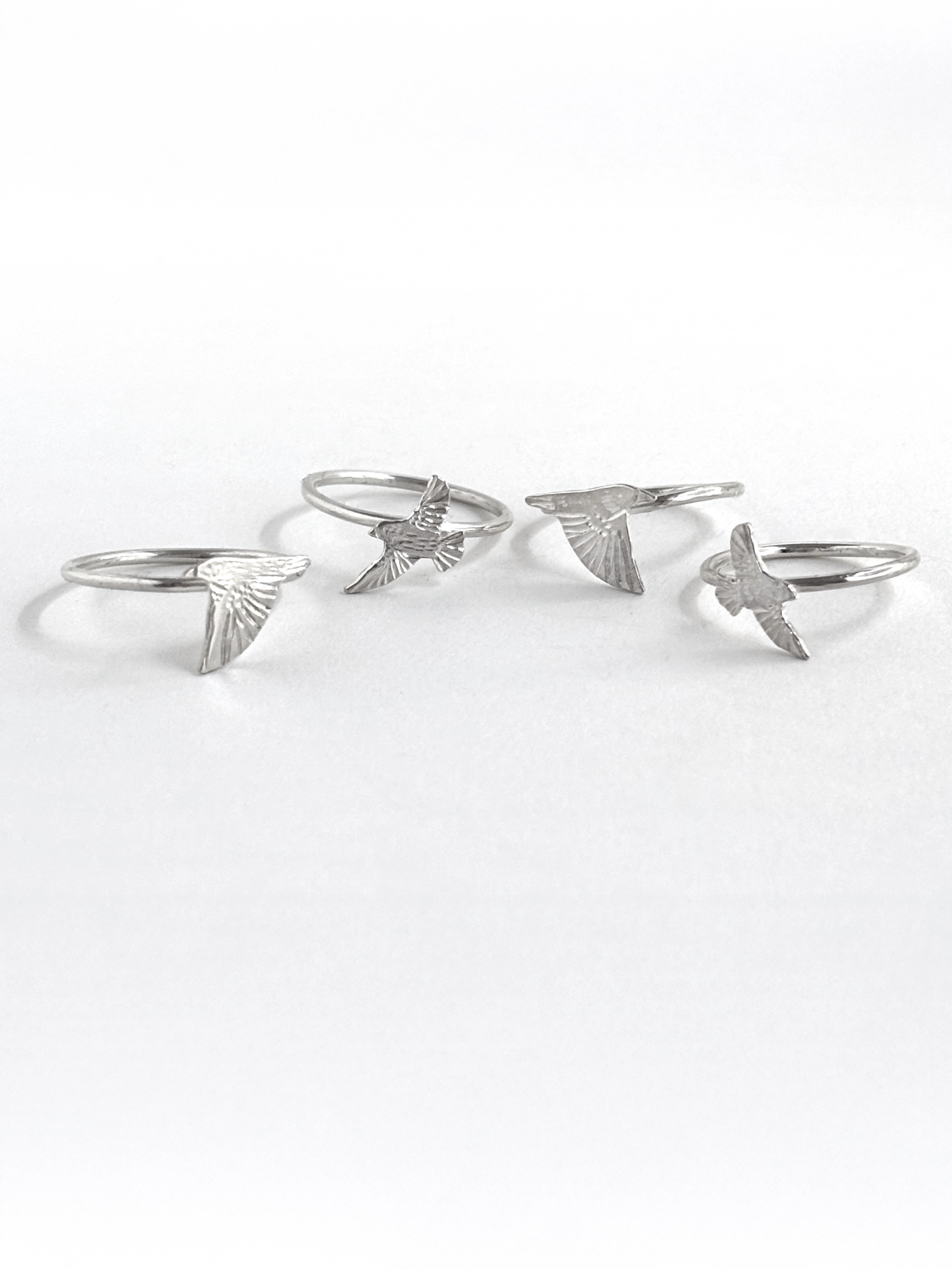 Four sterling silver starling rings laid out together, each an engraved starling in a different flying pose, on white