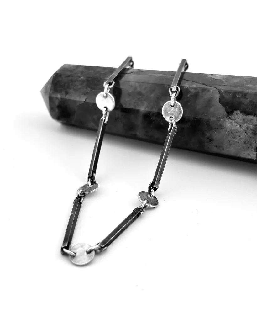Artisan handmade sterling silver bar and disc link bracelet designed by Stacy Bias Jewellery in Glasgow UK draped over a dark grey crystal point.