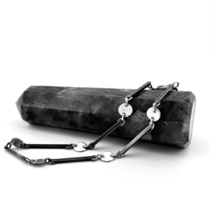 Handmade sterling silver bracelet featuring alternating thin metal bars and flat circular disc links draped over a dark crystal point.