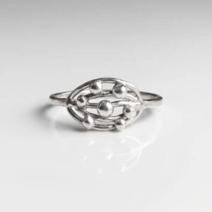 Close-up studio shot of the handmade sterling silver Orbit Cluster ring with reflective silver spheres inside an oval frame, resting on a white reflective surface.