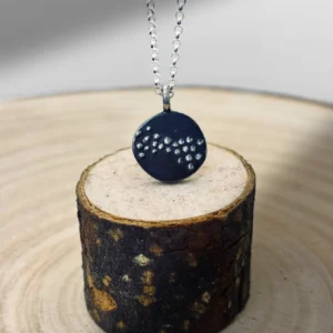 Murmuration Dot Flock Pendant resting on wood log with oxidised silver face and raised dots