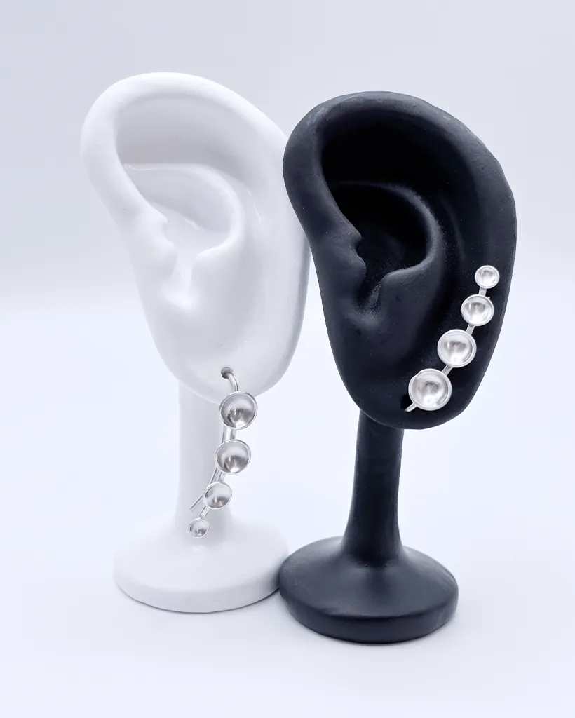 sterling silver ear climber earrings with four cascading dots from small to large. One is positioned to climb up the ear, one is rotated to dangle downwards.