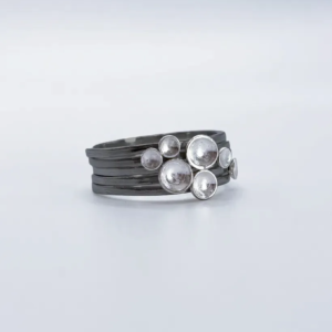Three-quarter view of the full oxidised sterling silver Murmuration Dot stacking ring set, polished dots clustered as a flock