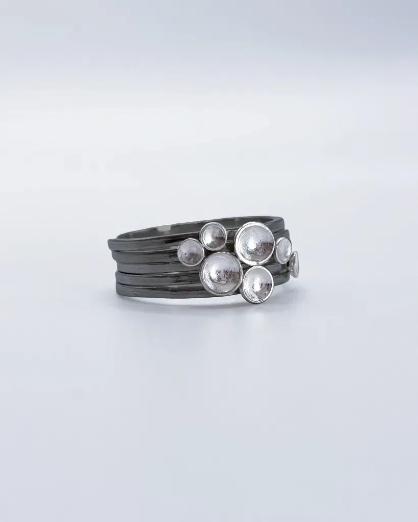 Three-quarter view of the full oxidised sterling silver Murmuration Dot stacking ring set, polished dots clustered as a flock