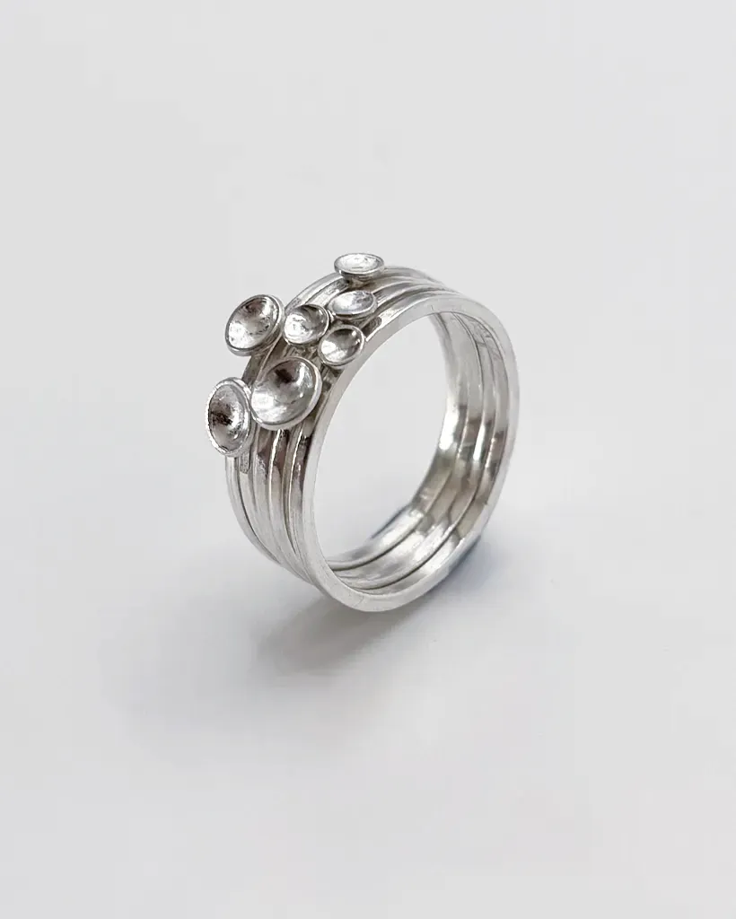 Polished sterling silver Murmuration Dot stacking rings at a high angle, five separate bands with domed dots on top