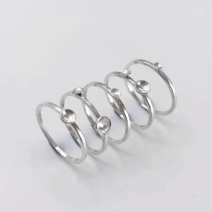 Five polished sterling silver Murmuration Dot stacking rings laid out separately, single dot and double dot bands