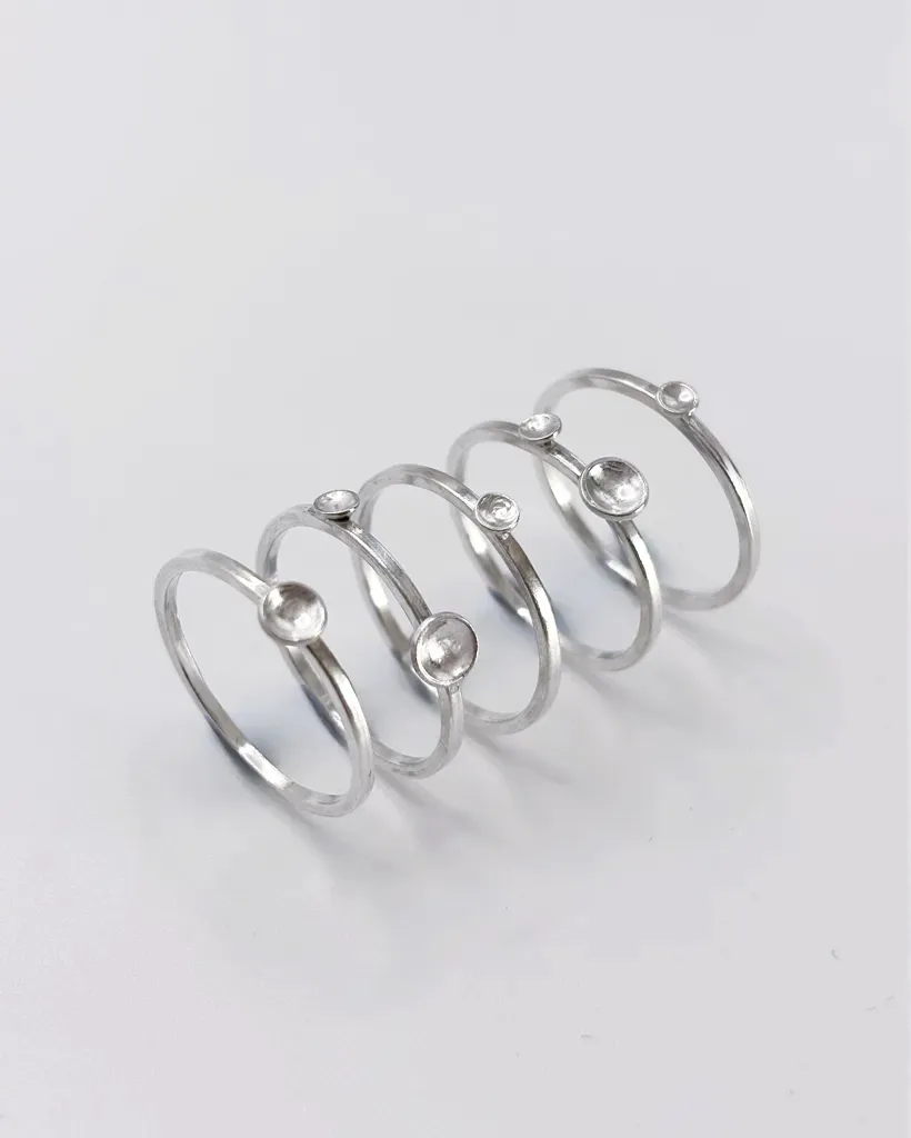 Five polished sterling silver Murmuration Dot stacking rings laid out separately, single dot and double dot bands