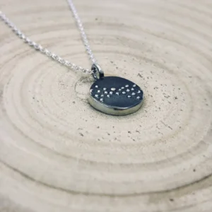 Angled view of the silver Murmuration Dot Flock pendant on a wood surface. Handcrafted by Stacy Bias.