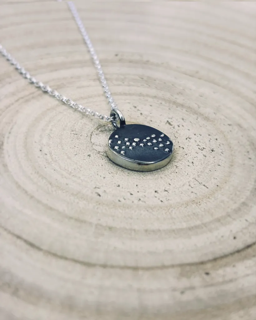 Angled view of the silver Murmuration Dot Flock pendant on a wood surface. Handcrafted by Stacy Bias.