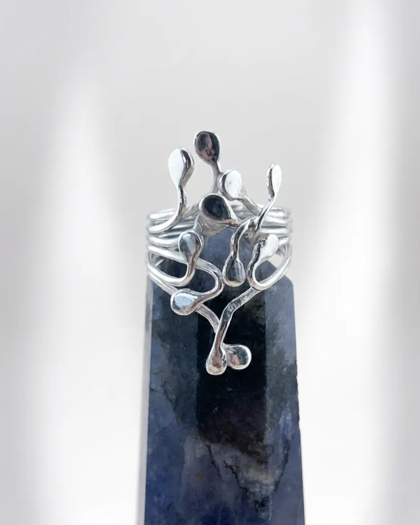 Artisan handmade sterling silver Squiggle ring with fluid, organic teardrop tendrils climbing from a multi-strand band, displayed on a dark crystal point.
