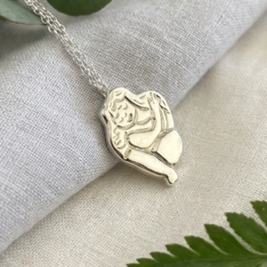 Chunky silver Self Love pendant on grey linen with green leaves. Sand cast necklace by Stacy Bias.
