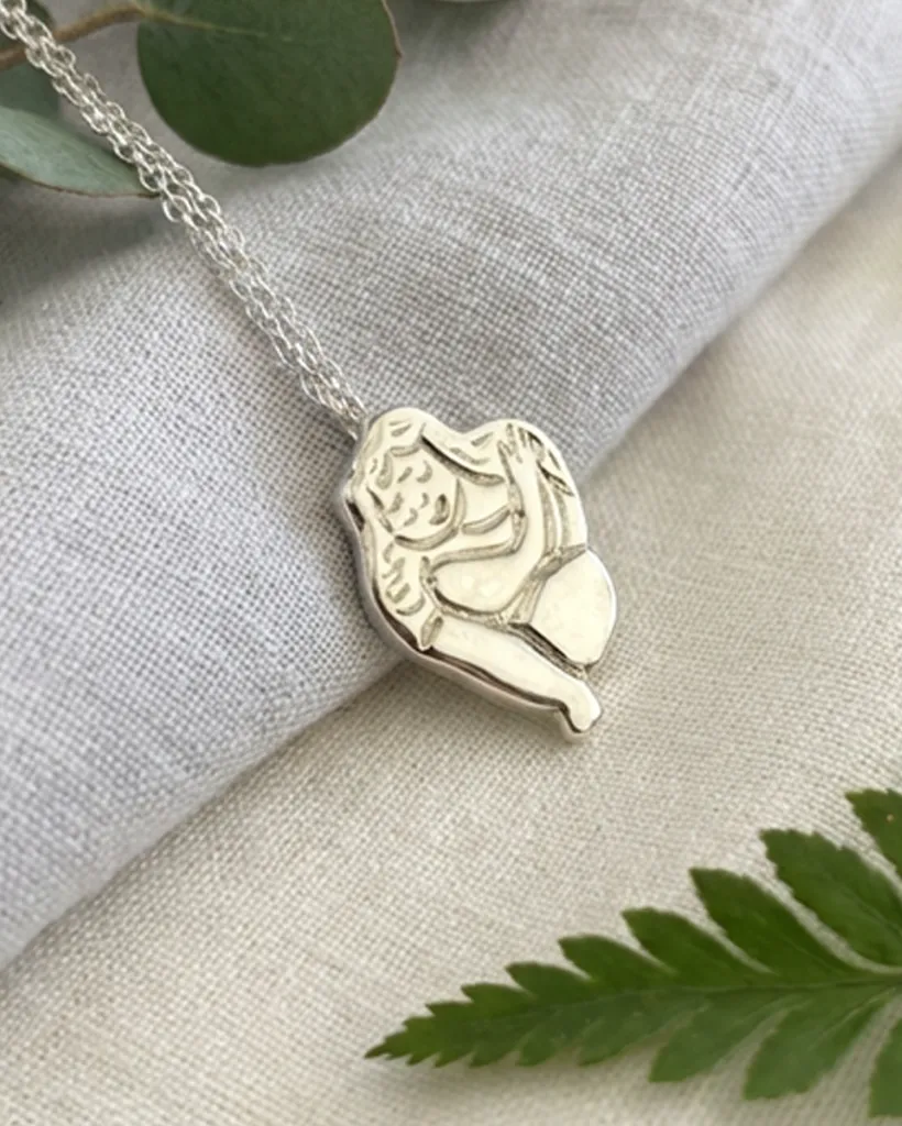 Chunky silver Self Love pendant on grey linen with green leaves. Sand cast necklace by Stacy Bias.