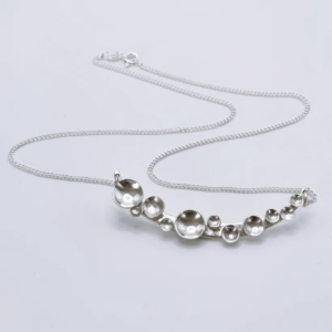 Bright silver Murmuration Dot Arc necklace with chain and clasp laid flat. Handcrafted by Stacy Bias.
