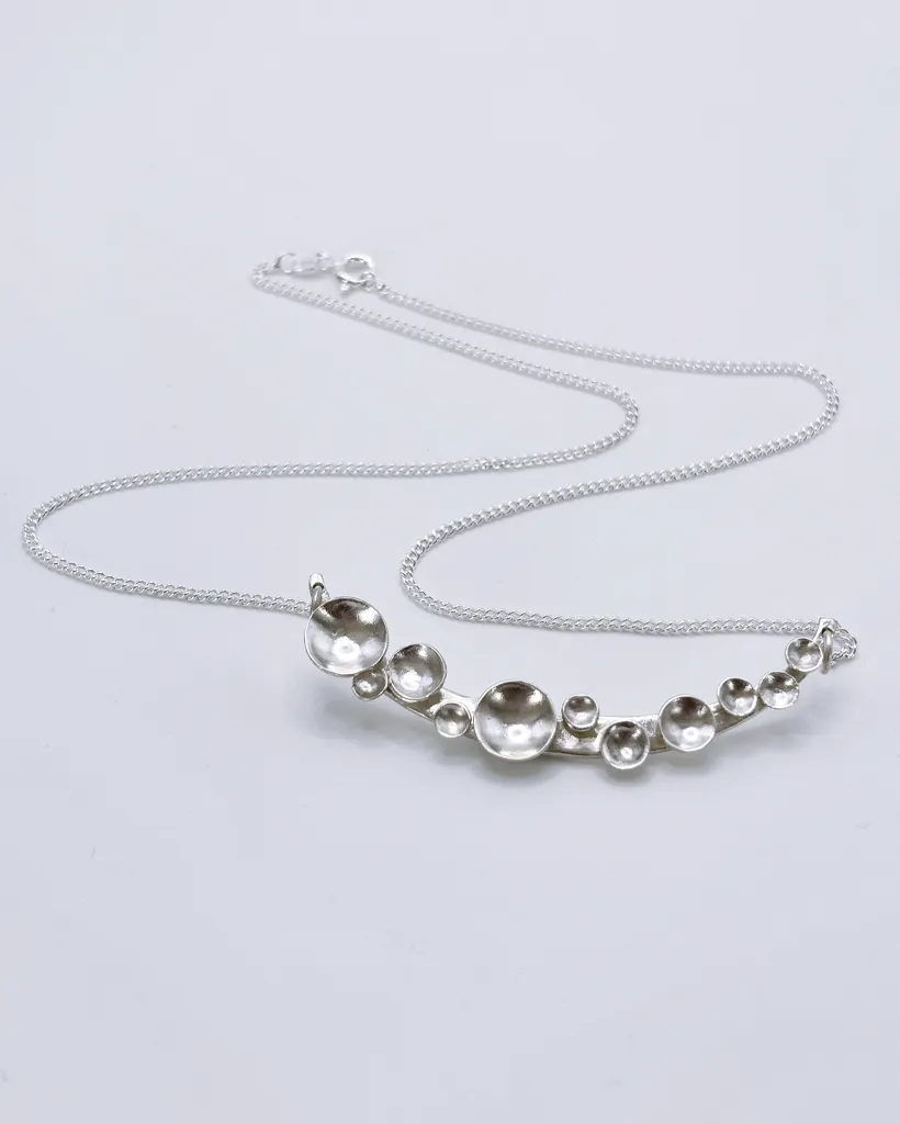 Bright silver Murmuration Dot Arc necklace with chain and clasp laid flat. Handcrafted by Stacy Bias.