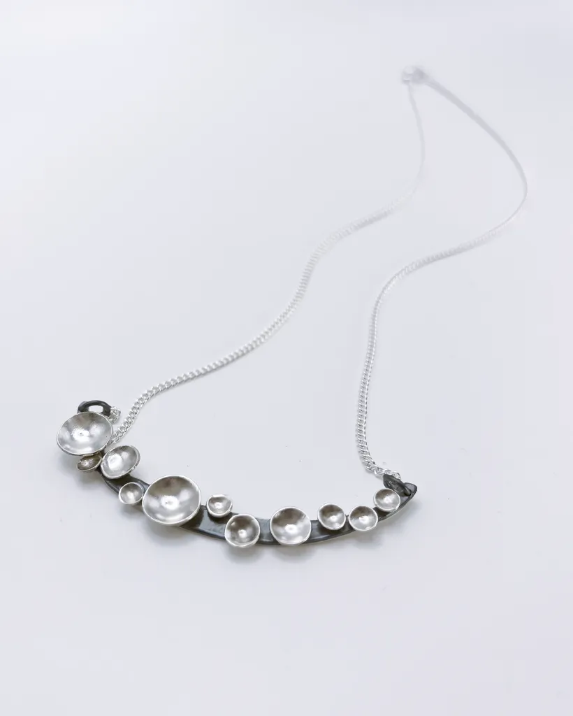Oxidised silver Murmuration Dot Arc pendant with polished domed dots on a fine chain. Handmade by Stacy Bias.