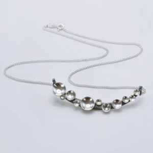 Oxidised silver Murmuration Dot Arc necklace with chain and clasp laid flat. Handcrafted by Stacy Bias.