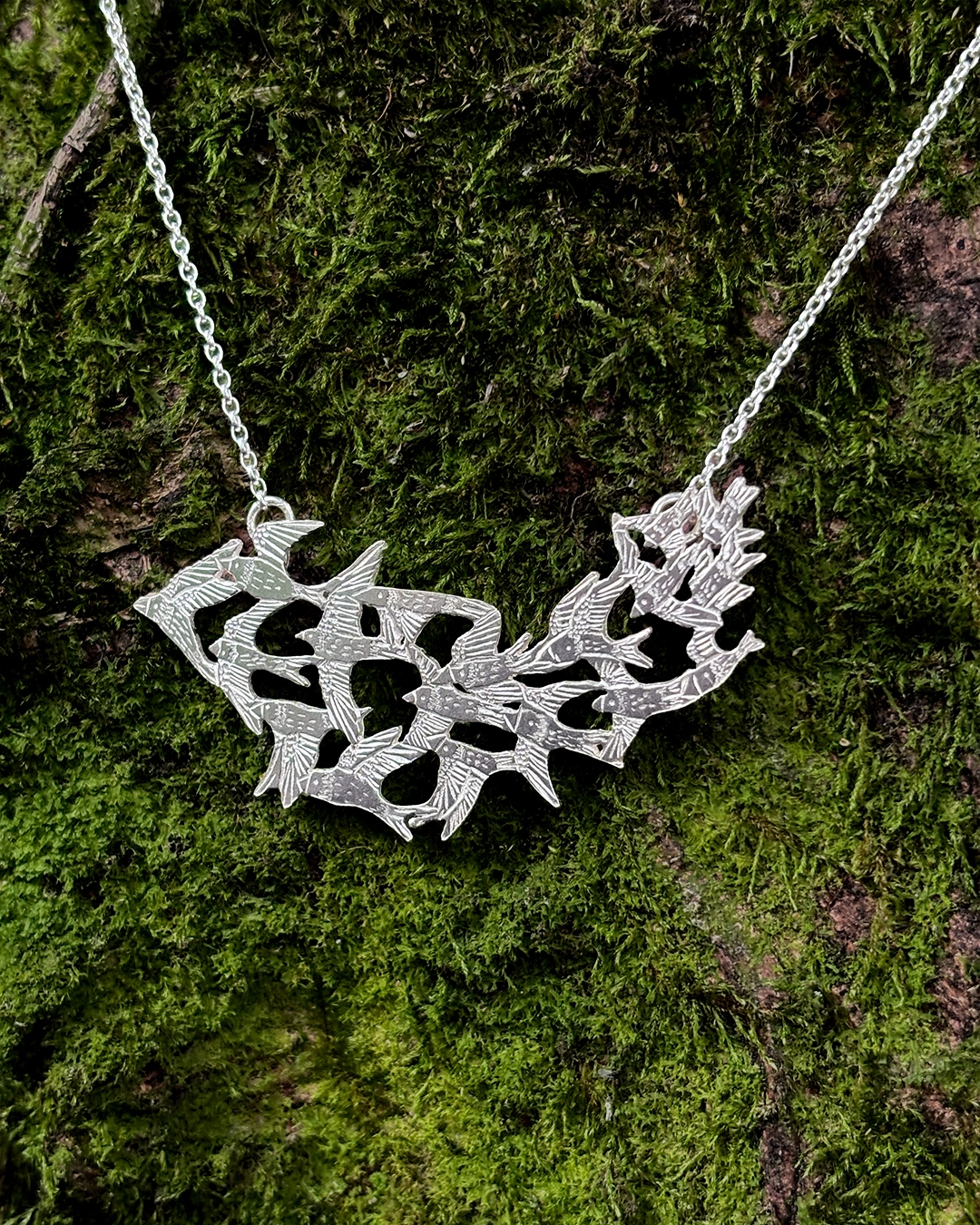 925 sterling silver statement necklace depicting a starling bird flock in flight, resting on rich forest floor foliage.