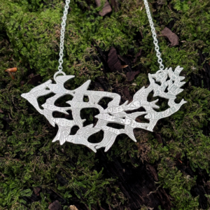 Closeup of hand-engraved 925 sterling silver bird murmuration necklace resting on textured forest moss.