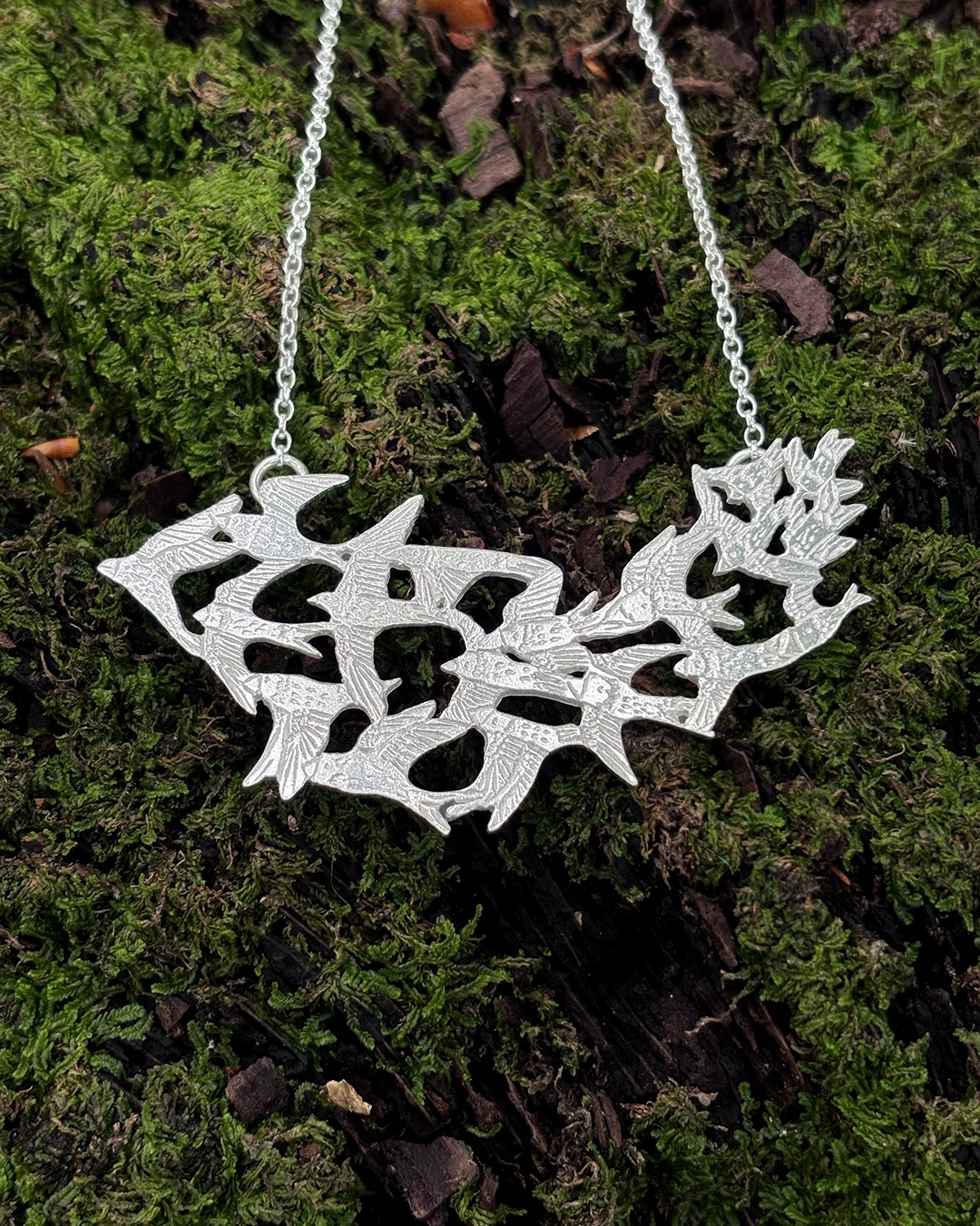 Handcrafted Silver Bird Murmuration Necklace - Stacy Bias Jewellery Closeup of hand-engraved 925 sterling silver bird murmuration necklace resting on textured forest moss.