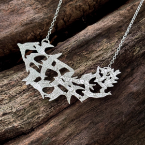 Angled closeup of a hand-pierced sterling silver statement necklace featuring a flock of starlings on a rustic wood log.