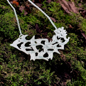 Diagonal view of the Scottish artisan silver murmuration necklace resting on moss-covered bark.