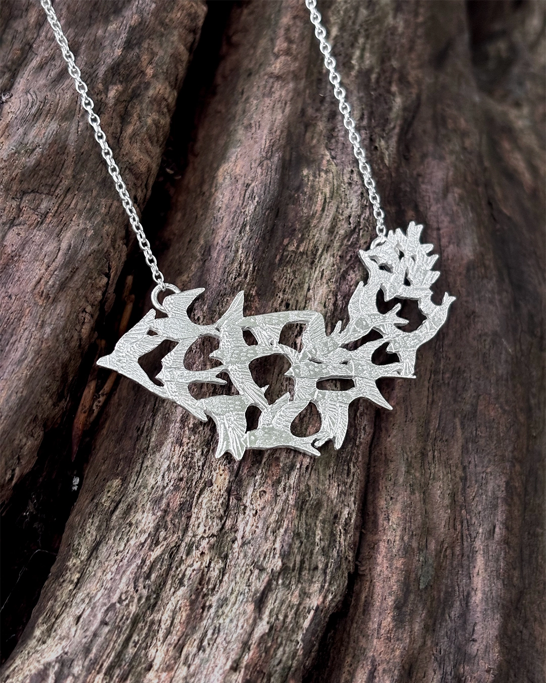 Fully detailed view of the handmade silver Murmuration necklace by Stacy Bias Jewellery over dark natural wood.